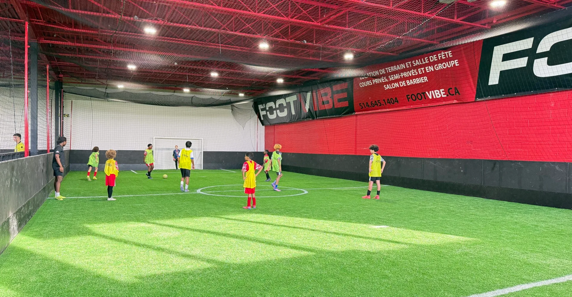 Vue panoramique du terrain intérieur FootVibe pendant une partie d'enfants en dossards, bannière FootVibe au mur