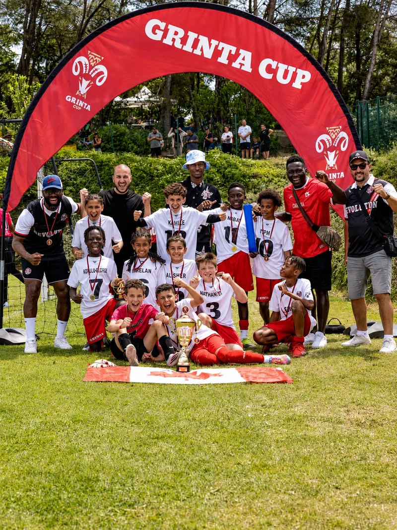 Équipe Révolution Football avec ses entraîneurs et une coupe sous l'arche de la Grinta Cup
