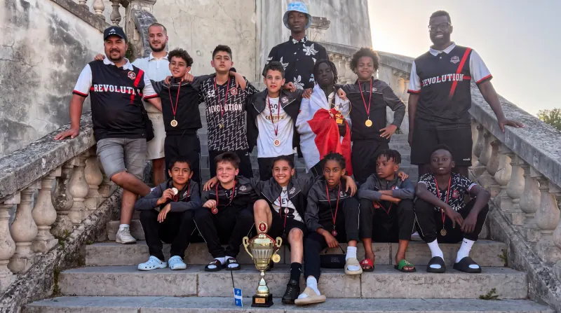 Équipe Révolution au complet, médailles au cou, posant avec le trophée sur les marches d'un escalier de pierre après un tournoi